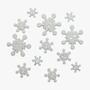May include: A collection of eleven white snowflake-shaped buttons with a glittery finish. Each button features a central design with two holes for sewing, varying in size from small to large, all arranged in a scattered pattern against a plain background.