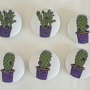 May include: Six round wooden buttons with a white background. Each button features a green cactus in a purple pot. The buttons have two holes for sewing. Great for sewing projects, crafts, and adding a decorative touch.