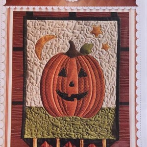 May include: A quilted wall hanging featuring a smiling jack-o'-lantern with a crescent moon and stars in the background. The title "Mr. Jack Wall Hanging" is printed below the image.
