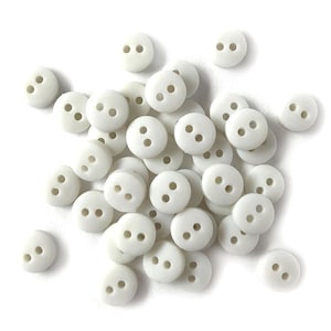 May include: A collection of small, round, off-white buttons with two holes each. The buttons are scattered across a white surface, creating a simple, clean aesthetic. These buttons are ideal for sewing and craft projects.