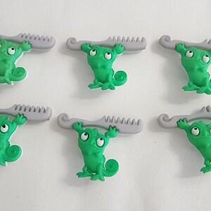 May include: Six green chameleon-shaped charms, each holding a gray comb. The chameleons have large eyes and curled tails. The combs are a light gray color. The charms are arranged in two rows of three.