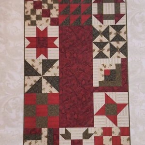 May include: A quilting pattern for a table runner called "Winterberry Table Scraps" with a red, green, and white color scheme. The pattern is 18 inches by 30 inches and is designed by The Prairie Grove Peddler, Cheryl Haynes.