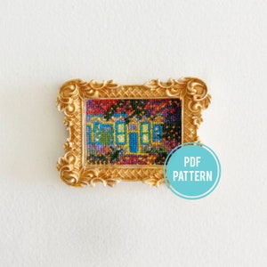 May include: A colorful cross-stitch pattern of a house with a blue door and windows, framed in a gold ornate frame. The text "PDF PATTERN" is on a blue circle.