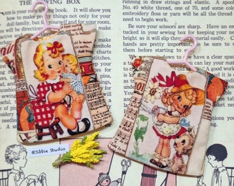 Puede incluir: Dos vestidos en miniatura para muñecas con estampado floral y notas musicales. Los vestidos están colgados de perchas rosas. Los vestidos están hechos de tela y tienen un aspecto vintage.
