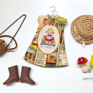 May include: A doll clothing set including a sleeveless dress with a vintage-style comic print and a central oval illustration of a girl, a brown crocheted round purse with a chain strap, brown lace-up boots, a straw hat, and a small mushroom.