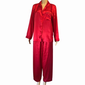 May include: A red satin pajama set. The set includes a long-sleeved button-down shirt with a chest pocket and matching pants. The fabric has a shiny appearance. The pajamas are displayed on a mannequin.
