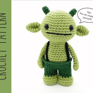 K&ouml;nnte beinhalten: Gr&uuml;nes geh&auml;keltes Amigurumi-Spielzeug mit schwarzen Augen und einem schwarzen Mund. Das Spielzeug tr&auml;gt eine gr&uuml;ne Hose mit schwarzen Hosentr&auml;gern. Das Spielzeug hat eine Sprechblase, in der steht: "Juhu! Du kannst mich selbst machen!"