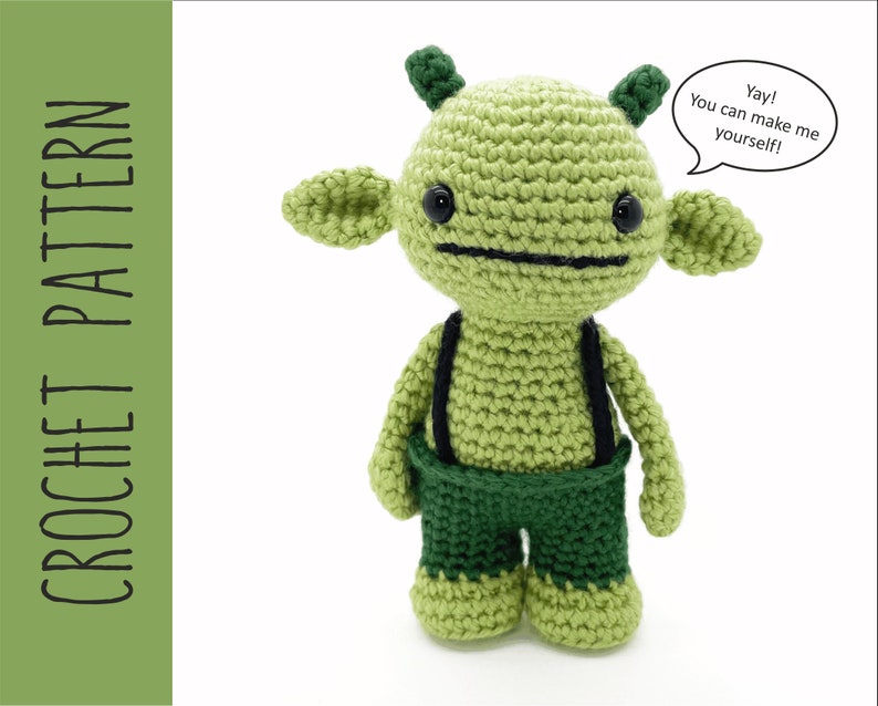 K&ouml;nnte beinhalten: Gr&uuml;nes geh&auml;keltes Amigurumi-Spielzeug mit schwarzen Augen und einem schwarzen Mund. Das Spielzeug tr&auml;gt eine gr&uuml;ne Hose mit schwarzen Hosentr&auml;gern. Das Spielzeug hat eine Sprechblase, in der steht: "Juhu! Du kannst mich selbst machen!"