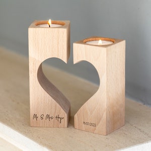 Puede incluir: Dos candelabros de madera con un recorte en forma de coraz&oacute;n, cada uno con una vela de t&eacute; encendida. Los candelabros est&aacute;n grabados con "Mr & Mrs Hope" y la fecha "14/07/2023".