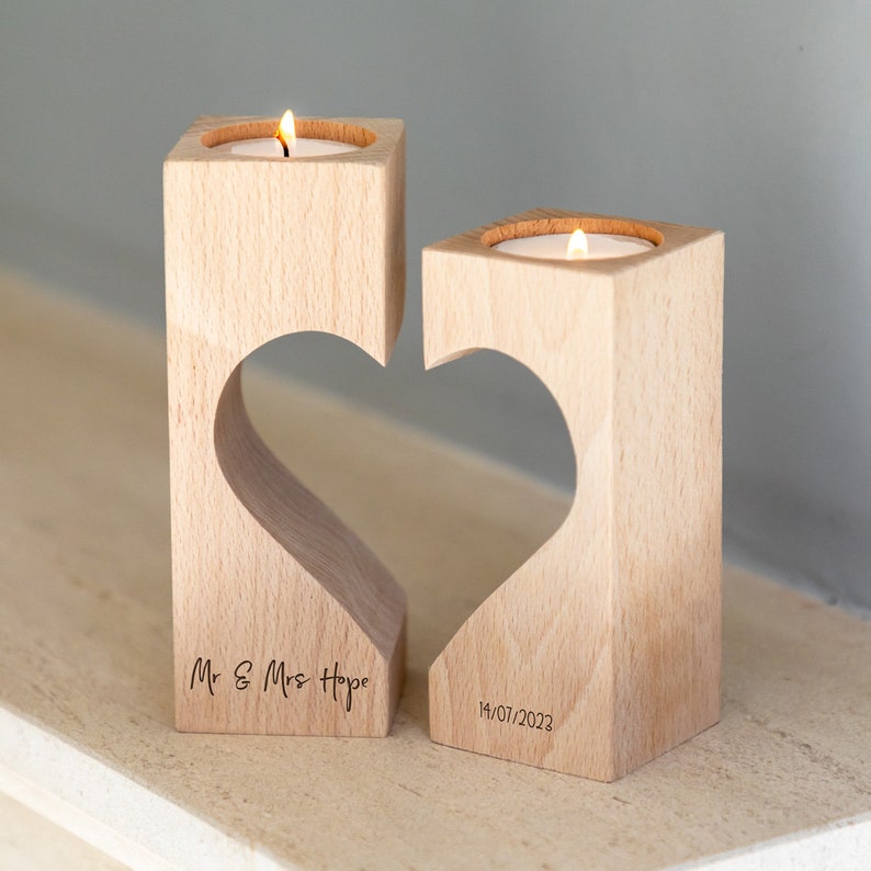 Puede incluir: Dos candelabros de madera con un recorte en forma de coraz&oacute;n, cada uno con una vela de t&eacute; encendida. Los candelabros est&aacute;n grabados con "Mr & Mrs Hope" y la fecha "14/07/2023".