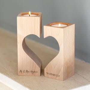 Puede incluir: Dos candelabros de madera clara con un recorte en forma de coraz&oacute;n. Cada uno tiene una vela encendida. Uno est&aacute; grabado con "Mr & Mrs Hopkins", el otro con "9th September 2024".