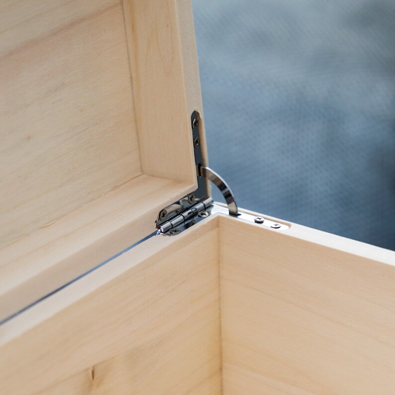May include: Close-up of a wooden box with a silver hinge. The box is made of light wood and has a smooth finish.