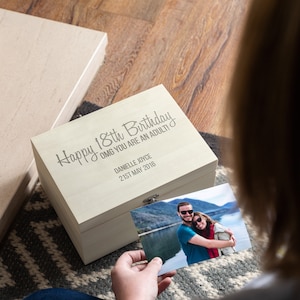 May include: A white wooden box with a hinged lid. The box is engraved with the text "Happy 18th Birthday OMG you are an adult!" and the name "Danielle Joyce" and the date "21st May 2016". A photo of a couple is in front of the box.