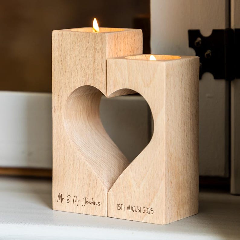 Puede incluir: Un portavelas de madera con un recorte en forma de coraz&oacute;n. Dos velas encendidas se colocan en los soportes. El texto "Mr & Mr Jenkins" y "15th August 2025" est&aacute; grabado. El portavelas es de madera clara.