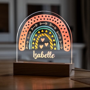 May include: A rainbow-themed night light with a wooden base. The rainbow is made of acrylic and features a colourful design with arrows, hearts, and triangles. The name "Isabelle" is written below the rainbow.