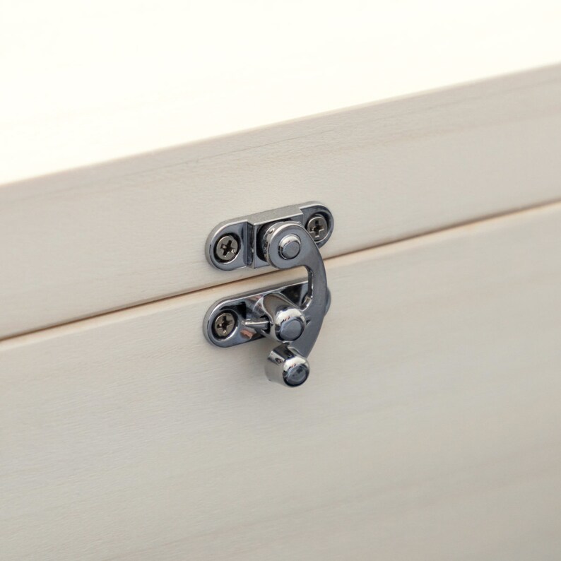 May include: A silver metal latch with two screws on a white wooden box.