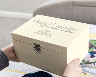 May include: A light wood keepsake box with a hinged lid and a silver clasp. The lid is engraved with the text "Happy Graduation It is official, you are a genius!" and "Eve Roberts BA (Hons) Marketing University of Bristol 2016".