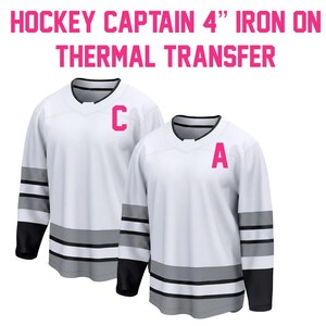 May include: Two white hockey jerseys with black and gray accents. One jersey has a pink "C" and the other has a pink "A". The text at the top reads "HOCKEY CAPTAIN 4" IRON ON THERMAL TRANSFER".