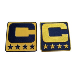 May include: Two embroidered patches featuring a navy blue letter "C" on a gold background. Each patch has four gold stars below the letter. The patches are square with rounded corners.