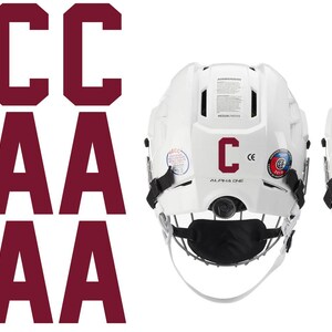 May include: White hockey helmets with black face masks and maroon letter decals. One helmet has a "C" decal, the other has an "A" decal. Maroon "C" and "A" letter decals are also shown.
