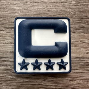 May include: A white patch with a navy blue letter "C" and four navy blue stars below it.