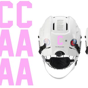 May include: Two white hockey helmets with black face masks. The letter "C" is on one helmet and the letter "A" is on the other. Pink letters "C" and "A" are also displayed on the left side of the image.