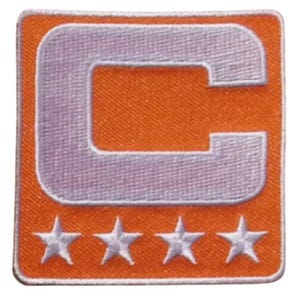 May include: Orange square patch with a white outline. The patch features a large, light purple letter "C" in the center and four white stars at the bottom. The patch has a textured appearance.