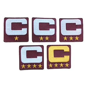 May include: Five embroidered patches featuring a capital letter "C" in white or gold, set on a maroon background. Each patch has a different number of gold stars below the letter, ranging from one to five stars. The patches are square.