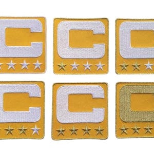 Peut inclure: Six écussons brodés avec un fond doré et un motif "C" blanc. Chaque écusson comporte cinq étoiles blanches en dessous du "C". Un écusson a un "C" doré.