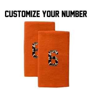 Peut inclure: Deux bracelets de poignet orange avec un numéro "6" à motif peau de serpent sur chacun. Personnalisez votre numéro.