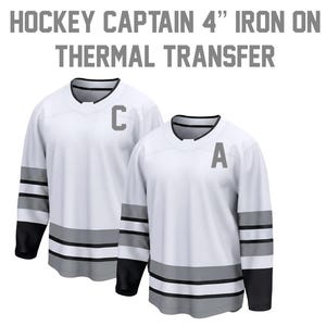 May include: Two white hockey jerseys with black and gray accents. One jersey has a gray "C" and the other has a gray "A". The text at the top says "HOCKEY CAPTAIN 4" IRON ON THERMAL TRANSFER".