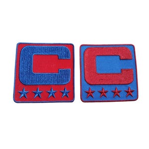May include: Two embroidered patches featuring a large letter "C" in red or blue, set against a contrasting background. Each patch has four embroidered stars at the bottom. The patches are square-shaped.