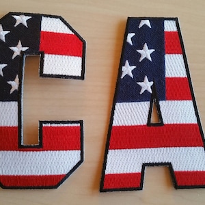 May include: Two felt patches in the shape of the letters C and A, with the design of the American flag. The patches are red, white, and blue.