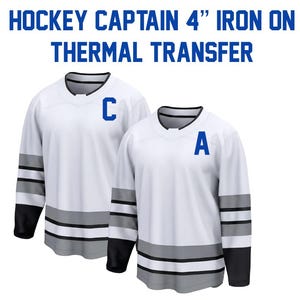 May include: Two white hockey jerseys with black sleeves, gray and black stripes, and blue letters. One jersey has a "C" and the other has an "A". The text "HOCKEY CAPTAIN 4" IRON ON THERMAL TRANSFER" is at the top.
