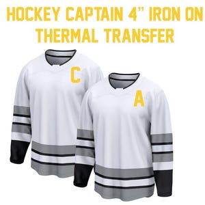 May include: Two white hockey jerseys with black and gray stripes on the sleeves and bottom. One jersey has a yellow "C" and the other has a yellow "A". Text at the top reads "HOCKEY CAPTAIN 4" IRON ON THERMAL TRANSFER."