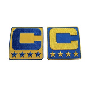 May include: Two embroidered patches featuring a yellow "C" inside a blue square, with four blue stars below. The background is yellow. The patches are likely for sports team apparel.