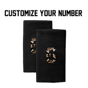 Peut inclure: Deux poignets noirs avec le chiffre "6" dans un motif peau de serpent. Le texte "PERSONNALISEZ VOTRE NUMÉRO" est au-dessus des poignets en lettres noires grasses. Sur fond blanc.