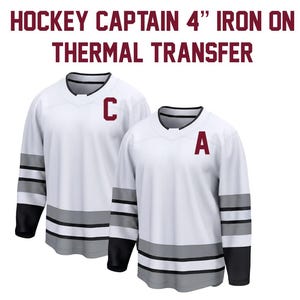 May include: Two white hockey jerseys with black sleeves and gray stripes. One jersey has a burgundy "C" and the other has a burgundy "A". The text at the top reads "HOCKEY CAPTAIN 4" IRON ON THERMAL TRANSFER."