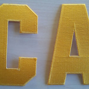 Peut inclure: Deux lettres en feutre doré, C et A, avec des coutures blanches autour des bords.