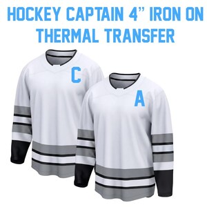 May include: Two white hockey jerseys with black and gray accents. One jersey has a light blue "C" and the other has a light blue "A". The text at the top says "HOCKEY CAPTAIN 4" IRON ON THERMAL TRANSFER".