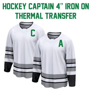 May include: Two white hockey jerseys with black and gray accents. One jersey has a green "C" and the other has a green "A". The text at the top reads "HOCKEY CAPTAIN 4" IRON ON THERMAL TRANSFER".