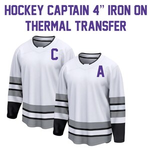 May include: Two white hockey jerseys with black sleeves and grey stripes. One jersey has a purple "C" and the other has a purple "A". Text at the top reads "HOCKEY CAPTAIN 4" IRON ON THERMAL TRANSFER."