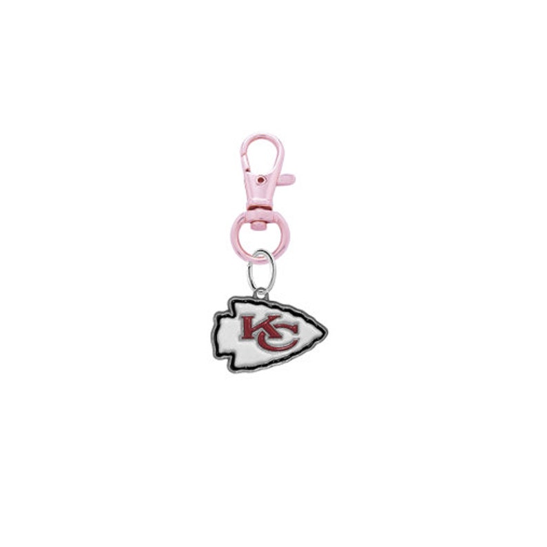May include: A pink metal keychain with a silver charm featuring the Kansas City Chiefs logo. The logo is a white arrowhead with a red "KC" inside.