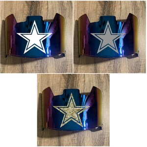May include: Three different color variations of a football helmet facemask with a white, gray, and camouflage star design. The facemask is iridescent blue and purple.