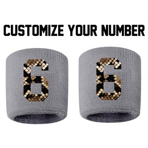 Peut inclure: Deux bracelets de poignet gris avec le chiffre 6 dans un motif peau de serpent. Le texte "CUSTOMIZE YOUR NUMBER" est au-dessus des bracelets en lettres noires en gras. Les bracelets sont en matière douce et absorbante.