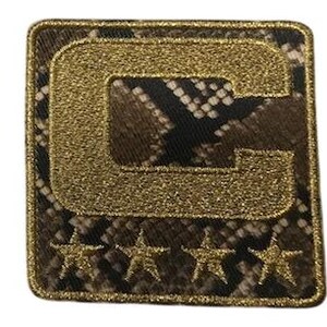 Puede incluir: Parche cuadrado con un fondo de estampado de piel de serpiente y una "C" dorada con purpurina en el centro. Cuatro estrellas doradas con purpurina en la parte inferior. El parche tiene un borde dorado.