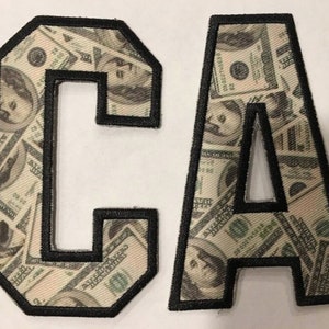 May include: Two felt patches in the shape of the letters C and A. The patches are covered in a pattern of US dollar bills.