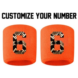 Peut inclure: Deux bracelets orange avec un motif de peau de serpent et le numéro "6" imprimé dessus. Personnalisez votre numéro.