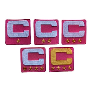 May include: Five embroidered patches with a pink background and a white or gold letter "C". Each patch has a different number of gold stars below the letter. The patches are square-shaped.