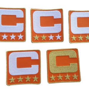 May include: Five orange patches with a white "C" and gold stars. The patches have a gold border. One patch has a gold "C". These patches are likely for sports team apparel.